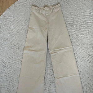 Beiga jeans från Zara   - Säljer ett par beiga jeans med breda ben och fransig kant nertill på benen från Zara i storlek 36. Jeansen har stora bakfickor och bälteshällor. 