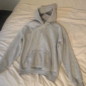 Grå hoodie med huva och ficka - En klassisk grå hoodie med huva och känguruficka framtill från bikbok.  Tröjan har långa ärmar, ribbade muddar och en avslappnad passform. Perfekt för chill dagar eller när du vill ha en enkel och stilren look.