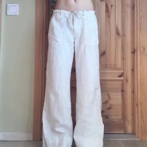 Vita linnebyxor med snörning - Snygga vita linnebyxor med relaxed fit och breda ben. Byxorna är lågmidjade, knytband i midjan och stora fickor med knappdetaljer både fram och bak. Perfekta för en chill och stilren look under varmare dagar🫶