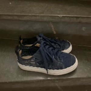 Chloé skor - Snygga mörkblå sneakers från Chloé med cool spetsdetalj och vit platt sula. Skorna har snörning och tydlig Chloé-logga baktill. Ovandelen är i textil med läckert mönster och läderdetaljer. Perfekta för dig som vill sticka ut med en unik och trendig look. Hyfsat slitna, men finns kvar att ge därav pris! 
