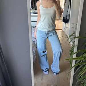 Ljusblå wide ripped jeans Bershka - Säljer ett par ljusblå jeans med bred passform och slitna hål på båda benen. Jeansen har klassisk femficksdesign, normal midja och är tillverkade i bomullsdenim. Perfekta för en avslappnad och trendig look.