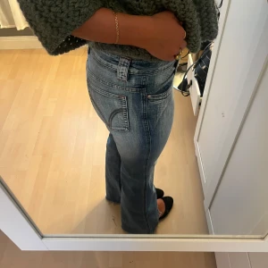  bootcut jeans ljusblå denim - Säljer ett par klassiska jeans i ljusblå tvätt med bootcut passform. Jeansen har hög midja, snygga kontrastsömmar och ikoniska bakfickor med bågen. Tillverkade i slitstark denim med lätt stretch för skön passform.