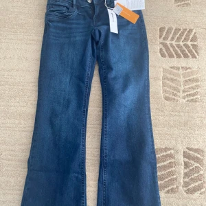 Bootcut jeans från Gina Tricot blå - Mörkblå bootcut jeans från Gina Tricot med låg midja. Klassisk femficksmodell med dragkedja och knapp framtill. Jeansen är tillverkade i stretchig bomullsdenim och har snyggt utsvängda ben för en trendig look.