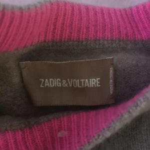 Brun stickad tröja med rosa stjärnor - Superfin brun stickad tröja från Zadig & Voltaire med coola rosa stjärnor över hela tröjan. Rund halsringning med ribbade muddar och nederkant. Perfekt för dig som vill sticka ut lite extra med en mysig och trendig look.