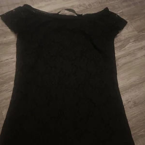 Svart tröja Black Label M - Supersnygg svart tröja från Black Label Collection i storlek M. Tröjan har ett vackert spetsmönster över hela tyget och korta ärmar. Perfekt för dig som vill ha en klassisk och stilren look med en touch av elegans.