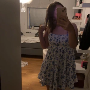 Vit och blå blommig klänning Shein - Supersöt kort klänning från Shein i vitt med blått blommönster. Klänningen har smala axelband, volangig kjol och en luftig passform. Perfekt för varma dagar och ger en fräsch look. Säljer då den aldrig kommer till användning, använd max 5 gånger. Väldigt somrig. 