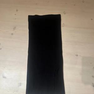 Svart långkjol i stretchigt tyg - En stilren svart långkjol med rak passform och stretchigt material. Kjolen är enkel och minimalistisk, perfekt för dig som gillar en clean look. Passar till sneakers eller boots för en cool vibe.