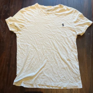 Vit t-shirt från Ralph Lauren - Vit t-shirt från Ralph Lauren med klassisk passform och liten broderad logga på bröstet. T-shirten har rund hals och korta ärmar, perfekt för en clean och enkel stil. Tillverkad i mjuk bomull som känns skön mot huden. Pass form passar även storlek S