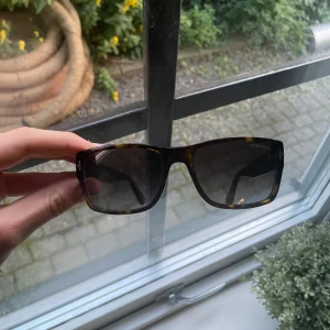 Tom Ford solglasögon brunmelerade - Snygga solglasögon från Tom Ford med fyrkantig form och brunmelerad båge. Glasen är mörka och ger en cool look. Perfekta för att lyfta din stil under soliga dagar. (Nypris cirka 3000kr)
