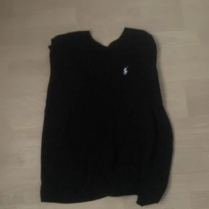 Svart tröja från Ralph Lauren - Svart tröja från Ralph Lauren med klassisk vit broderad logga på bröstet. Enkel och stilren design med rund halsringning. Perfekt för dig som gillar en clean och tidlös look.