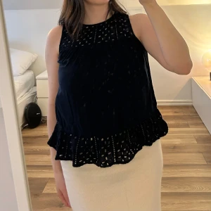 Mörkblå ärmlös blus - Säljer en mörkblå ärmlös blus från Vero Moda med fina broderade detaljer upptill och nertill. Blusen har volangkant nedtill och knytning i nacken. Perfekt för varma dagar! Välanvänd.