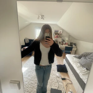 Svart croppad kofta från Divided - Säljer en svart, croppad kofta från Divided. Koftan har långa ärmar, v-ringning och knappar framtill. Den är stickad och passar perfekt till lager-på-lager-stil. Enkel att matcha med både jeans och kjol.