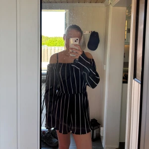 Marinblå randig offshoulder jumpsuit - Säljer en marinblå jumpsuit med vita ränder och offshoulder-design. Klänningen har långa ärmar och en smickrande passform med resår i midjan. Perfekt för sommarens alla tillfällen!