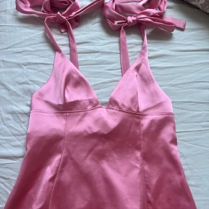 Rosa satin linne med knytband - Supersöt rosa linne i satin med v ringning och tunna axelband som knyts på axlarna. Har en lätt utsvängd passform och är perfekt för sommarens alla tillfällen. Säljes i storlek S. Ändasy provad och har prislappen kvar!! 