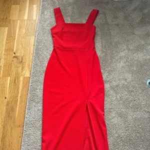 Röd långklänning med breda axelband - Säljer en snygg röd långklänning med breda axelband och rak halsringning. Klänningen har en figurnära passform och är perfekt för festliga tillfällen. Enkel och stilren design som verkligen sticker ut.