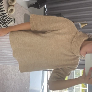 Trekvartsärmad tröja - Säljer en beige stickad polotopp med korta ärmar och lös passform. Enkel och stilren design som passar till det mesta. Knappt använd.
