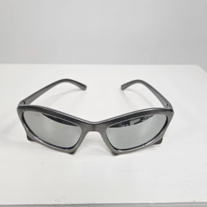 Metallic färgade sportiga solglasögon - Snygga metallic färgade solglasögon med spegelglas och sportig, futuristisk design. Bågarna är i plast och har en markerad, kantig form som ger en cool och modern look. Perfekta för dig som vill sticka ut med accessoarer.