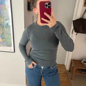 Grå ribbad långärmad topp från Zara - Säljer en grå ribbad långärmad topp från Zara. Tröjan har en tight passform och är tillverkad i ett mjukt, stretchigt material som sitter snyggt på kroppen. Perfekt att styla med jeans eller kjol.