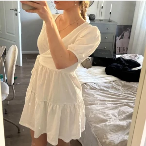 Vit kortklänning med v-ringning - Söt vit kortklänning med v-ringad hals och puffiga kortärmar. Klänningen har en volangkant nertill och är tillverkad i ett lätt material som passar perfekt till varma dagar. Enkel och stilren design som känns fräsch och somrig.💞💞