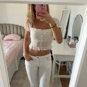 Vit spetsig croppad blus med volang - Säljer en söt vit croppad blus med spets och volangdetaljer. Blusen har korta puffärmar, knappar framtill och en fin v-ringning. 