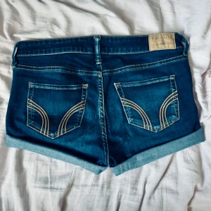 Mörkblå jeansshorts från Hollister - jag säljer ett par snygga jeans shorts med låg midja ifrån Hollister. Säljer pga att de ej kommer till användning längre. De är i mycket bra skick och har inga sorts skador eller hål. De är i waist 27, storlek XS/S. men passar även M. Perfekta för i sommar!!