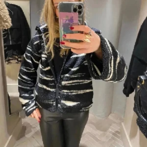 Svart och vit fleecejacka med dragkedja - Säljer en svart fleecejacka med vita zebraliknande ränder och dragkedja framtill. Jackan har hög krage och lång ärm, perfekt för kyligare dagar. Mjuk och skön med en lite oversized passform.