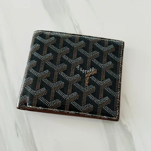 Svart brun plånbok  - Snygg svart brun plånbok med ikoniskt mönster i vitt och brunt. Plånboken har flera kortfack på insidan i brunt skinn och klassisk Perfekt accessoar för dig som vill ha något stilrent och exklusivt.