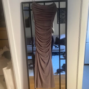 Lång axelbandslös klänning i taupe - Säljer en elegant axelbandslös långklänning i taupe med draperad effekt längs hela klänningen. Snygg passform som framhäver siluetten och ger en lyxig känsla, svår att få fin på bild. Perfekt för speciella tillfällen. Aldrig använd.