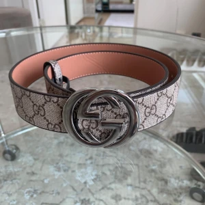 Beige GG Supreme bälte  - Säljer ett beige bälte Supreme-mönster och stor silverfärgad GG-logga som spänne. Bältet har en lyxig känsla och är fodrat med ljusrosa skinn på insidan. Perfekt accessoar för att lyfta din outfit.