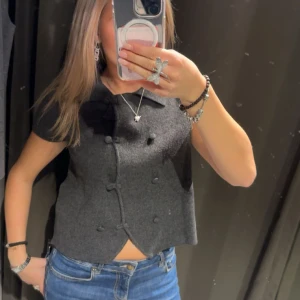 Mörkgrå tröja med knappar - Stilren mörkgrå t-shirt med dekorativa knappar framtill och lätt v-ringad hals. Från Zara och bara använd några gånger. Ge prisförslag 