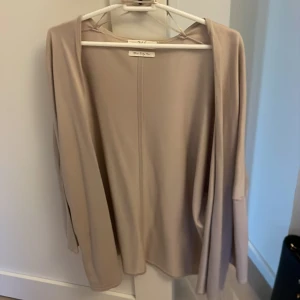 Beige kofta från 365 - Säljer en stilren och tunn beige kofta från 365. Koftan har öppen front utan knappar och långa ärmar. Perfekt att slänga över en topp för en enkel och snygg look.