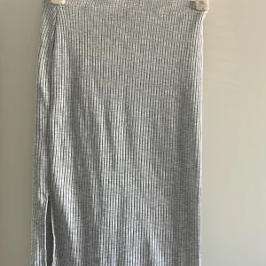 Grå ribbad långkjol - Säljer en grå ribbad långkjol med smal passform. Kjolen har ett diskret vertikalt ribbmönster och är tillverkad i ett mjukt och stretchigt material som känns bekvämt mot huden. Perfekt att styla med en enkel topp eller hoodie.