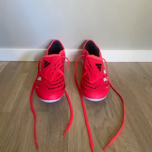 Adidas Predator fotbollsskor i röd och svart - Säljer ett par Adidas Predator fotbollsskor i en riktigt snygg röd färg med svarta och vita detaljer. Skorna har snörning och en sportig design med mönstrade detaljer på ovandelen. De är använda en gånga och är perfekta för dig som vill sticka ut på planen! ( Är den dyraste modellen kommer inte ihåg vad de heter)