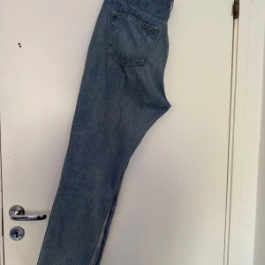 Blå jeans från Weekday - Säljer ett par klassiska blå jeans från Weekday med raka ben och normal passform. Byxorna har fem fickor, knappar i gylfen och är tillverkade i bomull. Perfekta för en avslappnad stil.