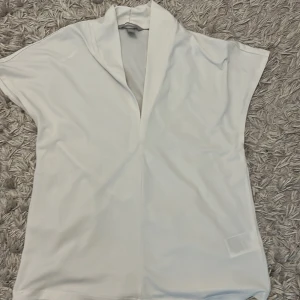 Vit blus med v-ringning från H&M - Säljer en stilren vit blus från H&M i storlek XS. Blusen har en djup v-ringning och korta ärmar, perfekt för en enkel och fräsch look. Tillverkad i ett mjukt och lätt material.