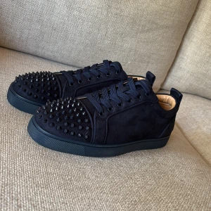Christian Louboutin  - Säljer ett par mörkblåa sneakers i mocka från Christian Louboutin med coola nitar på tån och den ikoniska röda sulan. Skorna har snörning och rund tå, perfekt för dig som vill sticka ut med din stil.