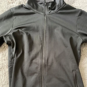 Svart jacka med dragkedja från SOC - Svart jacka från SOC med hel dragkedja framtill och hög krage. Jackan har långa ärmar och praktiska fickor med dragkedja. Perfekt för dig som vill ha en enkel och stilren jacka till vardagen.