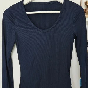 Mörkblå ribbad långärmad topp - Säljer en mörkblå långärmad topp med rund halsringning. Tröjan är ribbad och har en tight passform, perfekt att styla till olika outfits. Enkel och stilren design som passar till mycket.