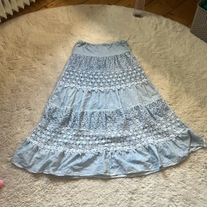 Ljusblå långkjol med spets och volang - Säljer en ljusblå långkjol. spetsdetaljer och volang längst ner. Kjolen har ett romantiskt och bohemiskt uttryck med broderade partier och mjukt fall. Perfekt för dig som gillar en feminin och avslappnad stil. Perfekt till en mysig sommar kväll. 