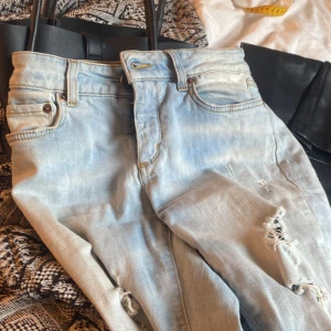 Ljusblå slitna jeans - Ljusblå jeans med slitningar och hål på benen. Klassisk femficksmodell med dragkedja och knapp framtill. Jeansen har en rak passform och är perfekta för en avslappnad stil.