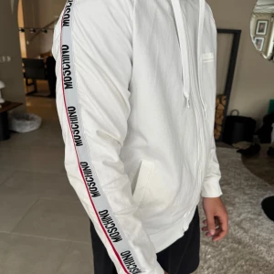 Vit zip-hoodie från Moschino - Säljer en vit hoodie med dragkedja från Moschino. Knappt använd, riktigt fin hoddie som passar till allt ! 