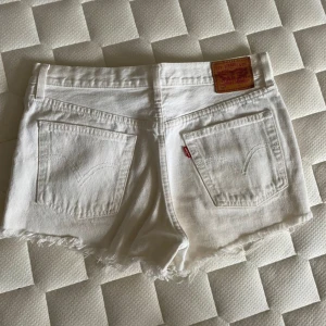 Vita jeansshorts - Levi's 501 - Säljer ett par vita jeansshorts från Levi's 501 med fransig kant och slitna detaljer framtill. Klassisk femficksmodell med knappgylf och läderpatch bak. Perfekta för sommaren! Passar xs-m beroende på vilken passform man vill ha. Säljer pga att jag skaffat andra shorts och behövde gå igenom garderoben… Skriv vid minsta frågor och funderingar.☺️