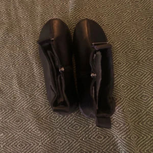 Svarta fodrade stövlar med dragkedja - Säljer ett par svarta stövlar med dragkedja på insidan och mjukt vitt foder. Skorna har platt sula och är perfekta för kyligare dagar. Klassisk design som passar till många outfits.