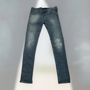 Blå Replay Jondrill jeans - Säljer ett par blå Replay Jondrill jeans med slitna detaljer och klassisk femficksdesign. Jeansen har en smal passform och är tillverkade i denim med lätt tvättad look. Perfekta för dig som gillar en modern och stilren stil. Skriv vid eventuell frågor 