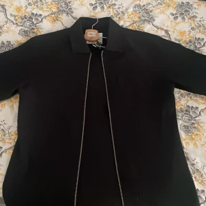 Svart jacka från Jack & Jones - Säljer en stilren svart jacka från Jack & Jones Premium med hel dragkedja framtill och klassisk krage. Perfekt för dig som gillar enkel och clean design. Jackan är lätt och passar bra till många olika outfits.