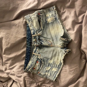 Ljusblå slitna jeansshorts - Säljer ett par ljusblå jeansshorts med slitna detaljer och fransig kant. Shortsen har klassisk femficksdesign och låg midja. Perfekta för varma dagar och en avslappnad stil. strl xs/s(står inget i de). köpte i cypern.