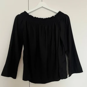 Svart offshoulder blus - Säljer en svart offshoulder blus med långa ärmar och smockad resår upptill. Lös passform och tunt material. Kan bäras upp på axlarna också.