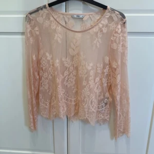 Ljusrosa spetsblus från ONLY - Säljer en ljusrosa, transparent spetsblus från ONLY i storlek 38. Blusen har lång ärm och vackert blommigt spetsmönster. Perfekt att styla över ett linne eller bh för en trendig look.