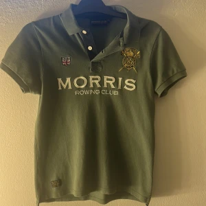 Grön pikétröja från Morris Rowing Club - Snygg grön pikétröja från Morris Rowing Club med broderade detaljer och tryck framtill. Klassisk krage med knappar och korta ärmar. Perfekt för en sportig och stilren look.