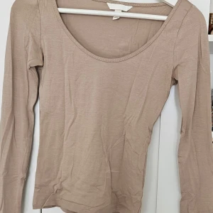 Beige långärmad topp med rund hals - Säljer en enkel och stilren beige långärmad topp med rundad halsringning från H&M. Perfekt att matcha med jeans eller kjol för en clean look. Tunn och mjuk i materialet, passar året runt.